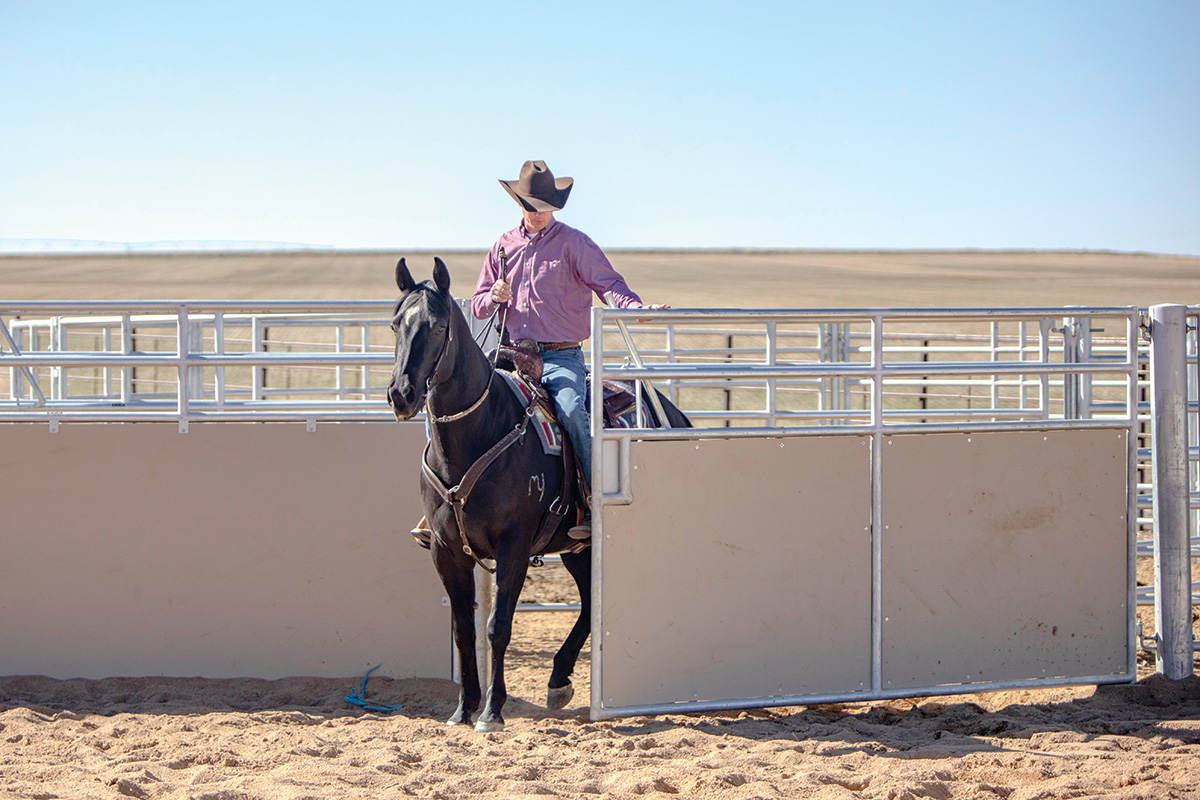 A trainer riding a horse through a gate on a ranch