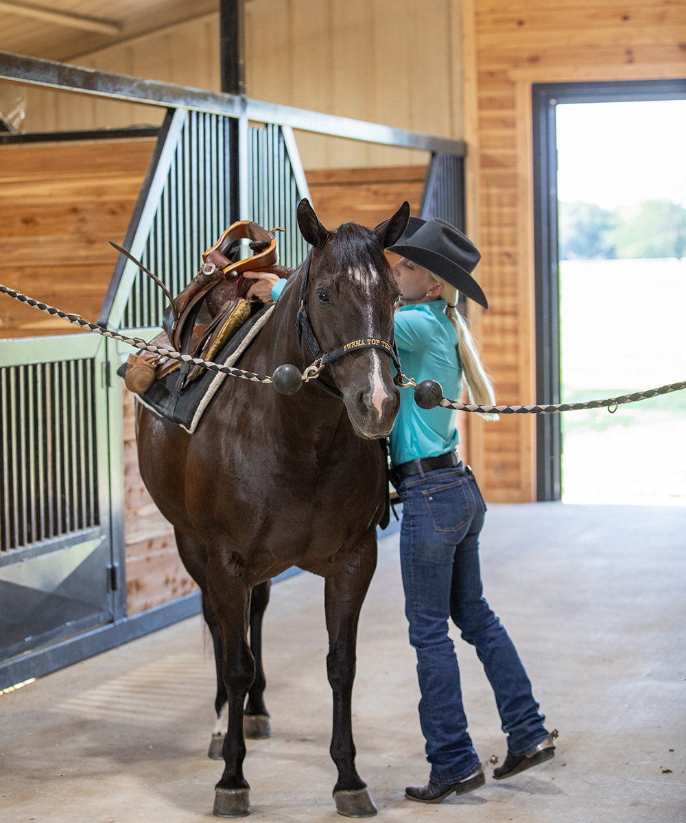 A woman saddles up her horse in a clean barn aisle. A cluttered barn aisle is a mistake beginners should avoid.