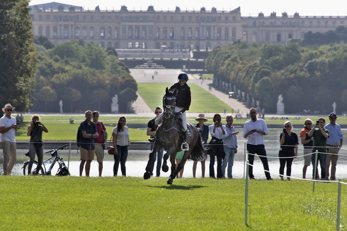 An horse and an equestrian on course with the Palace of Versailles in the background