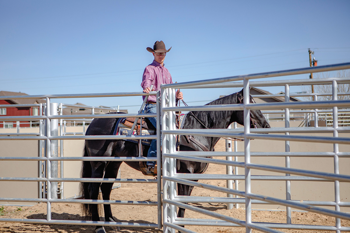 A trainer approaches a fence aboard a black gelding