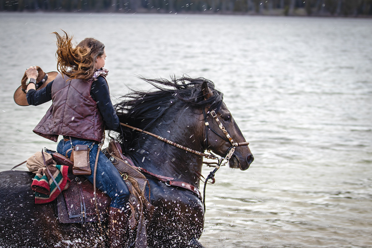 A woman galloping a large brown gelding through the water