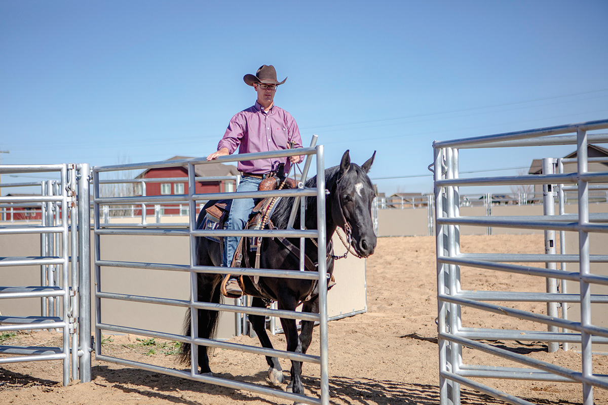 A trainer maneuvers his horse through a gate on a ranch