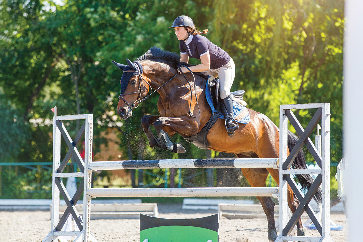 An equestrian clearing a high jump, which requires goal setting to achieve.