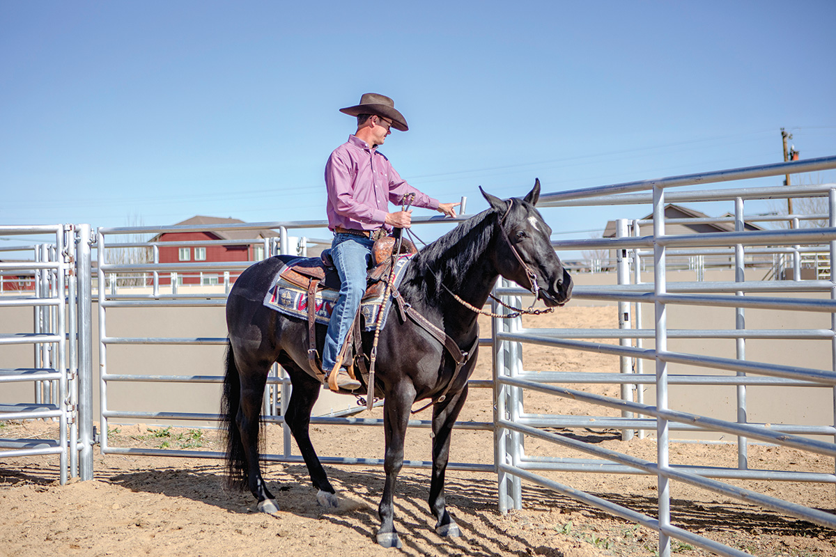 A trainer closes a ranch gate after riding a horse through it