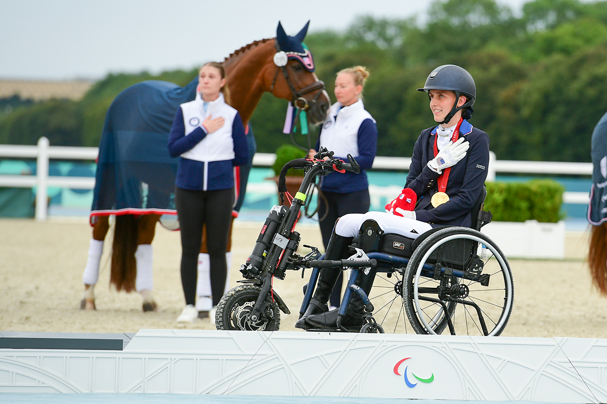 Fiona Howard celebrates the presentation of the United States' national anthem on the podium, with Diamond Dunes and team alongside